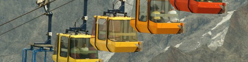 Four aerial tramway cars going up the side of a slightly snow covered mountain.