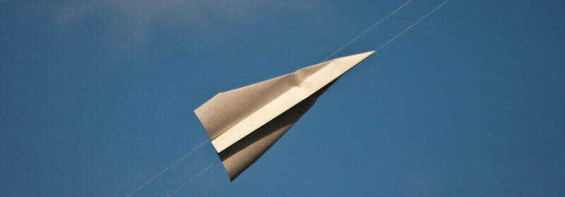 Paper plane flying through blue sky