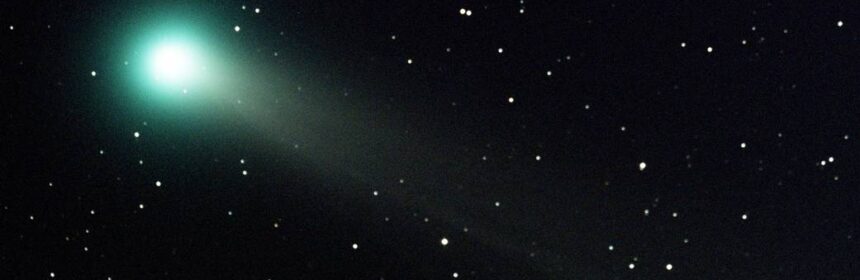 A photo of a comet with a green haze surrounding, with stars around