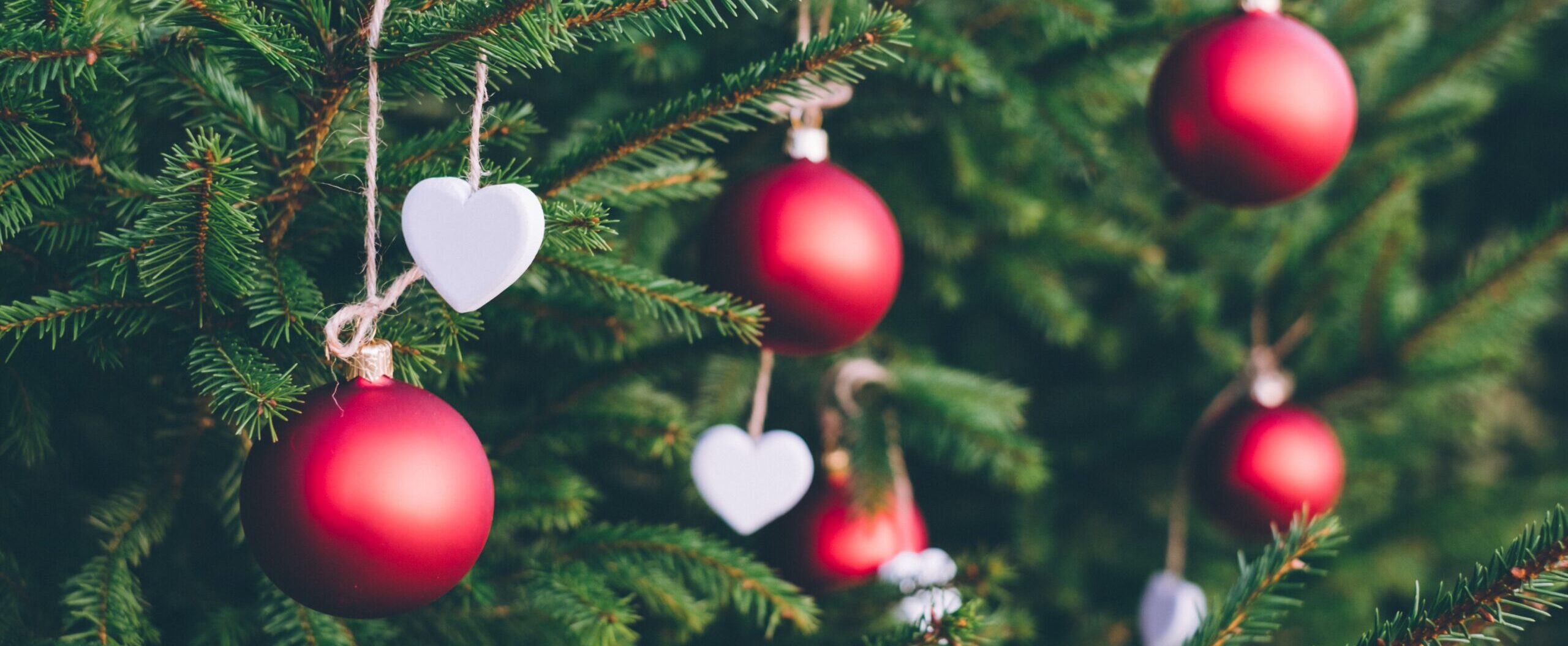 Close up of red baubles and white hearts hanging on Christmas tree
