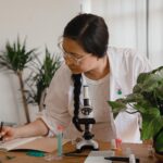 Woman researcher conducting research and taking notes with microscope and plants.