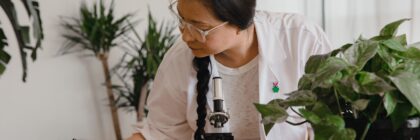Woman researcher conducting research and taking notes with microscope and plants.
