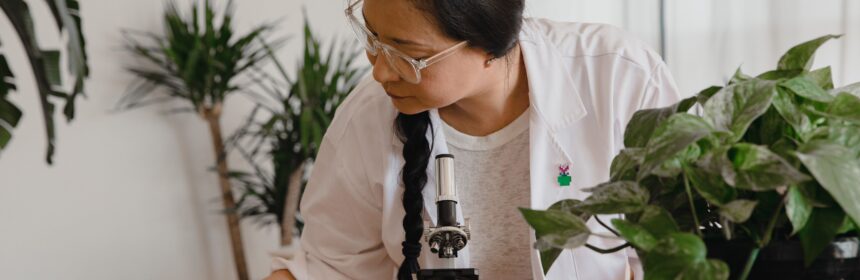 Woman researcher conducting research and taking notes with microscope and plants.
